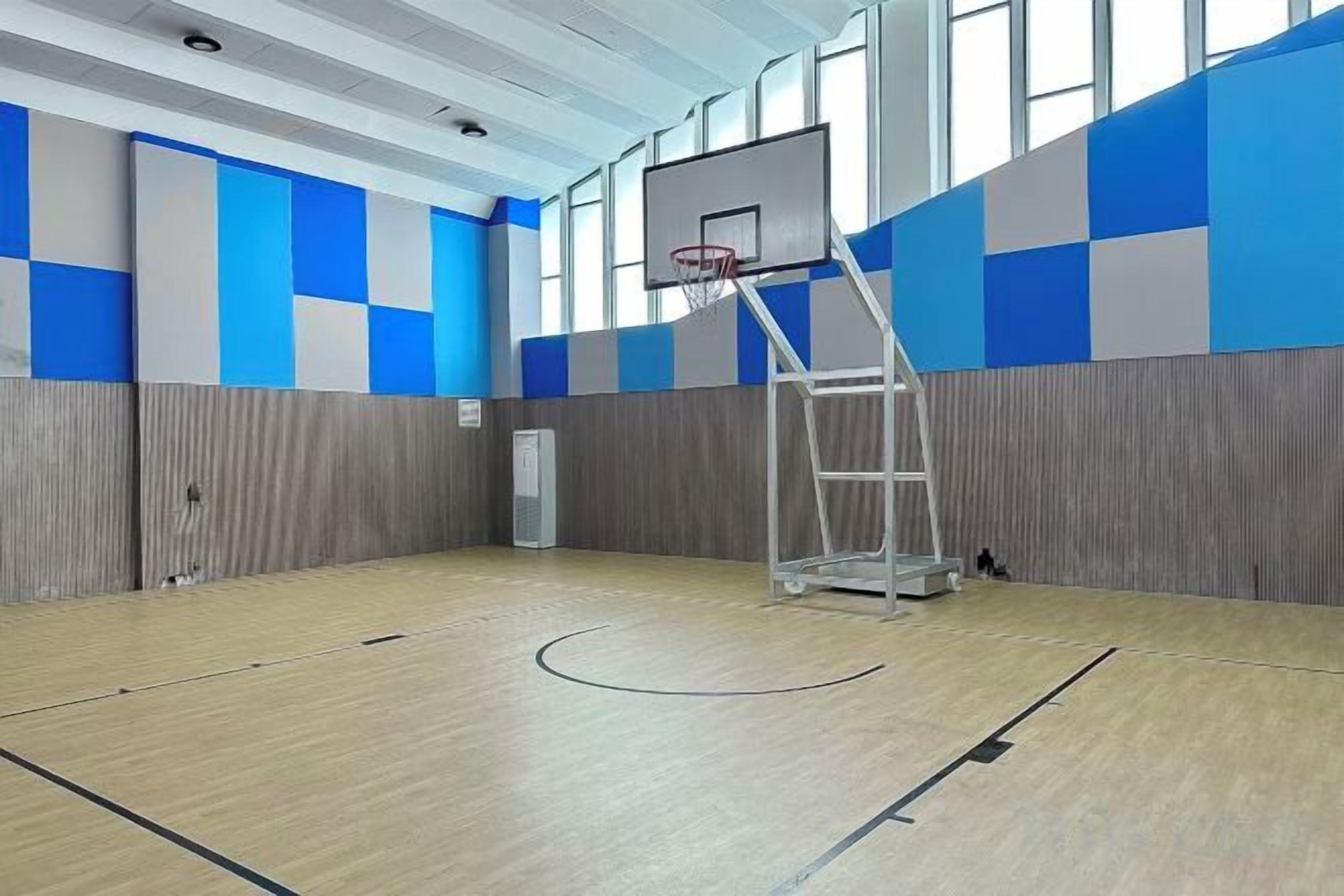 An indoor basketball court with a basketball hoop, a ladder, and a wall with blue and gray panels.