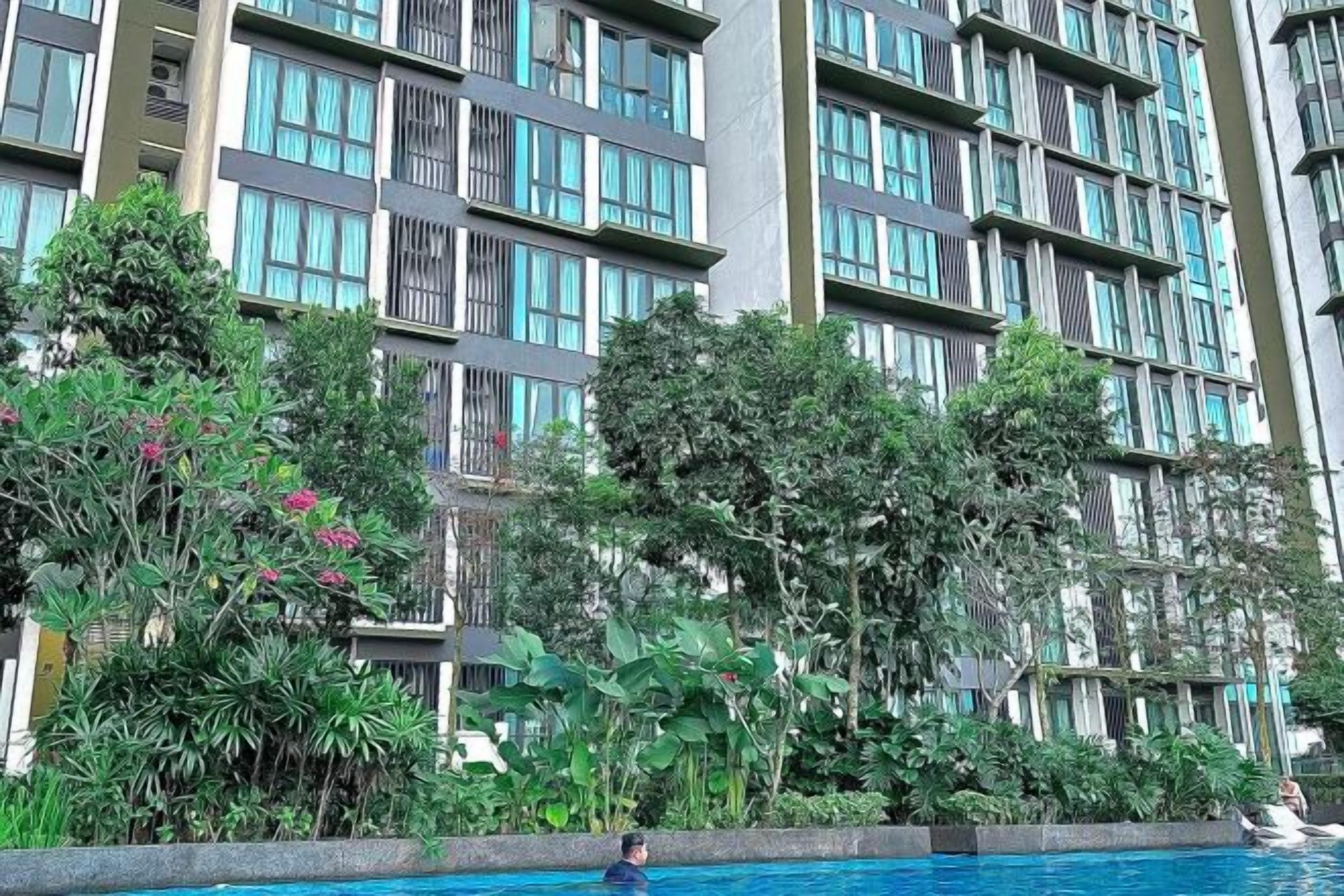 A multi-story building with a swimming pool, surrounded by lush greenery and trees.