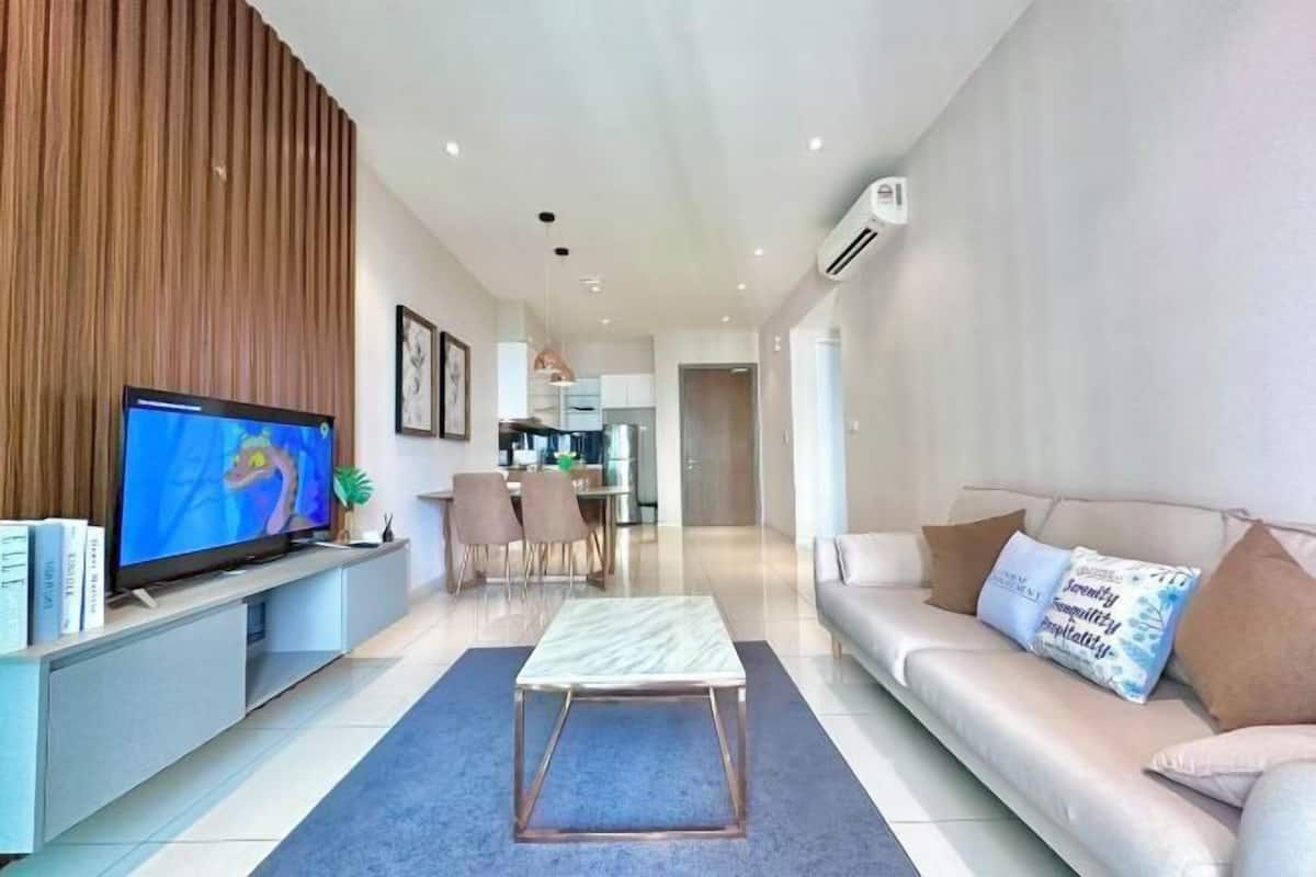 A modern living room with a flat-screen TV, a sofa, a coffee table, and a dining area in the background.