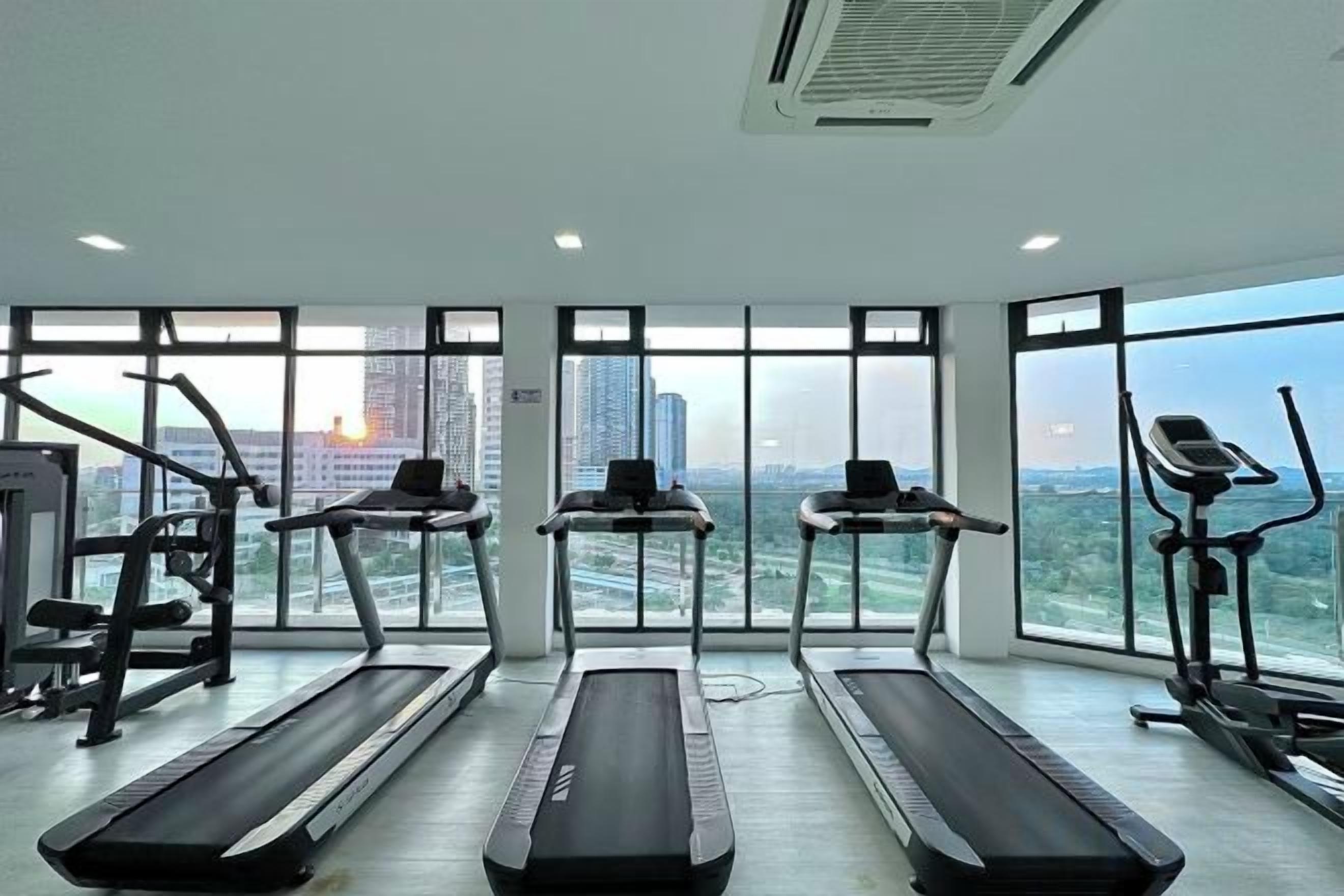 A gym with treadmills and exercise equipment, large windows with a city view.