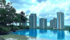 A swimming pool with lounge chairs, surrounded by greenery and tall residential buildings in the background. - Elysia Park Medini by Stayrene near Legoland (Iskandar Puteri)