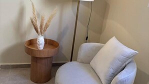 A room with a round wooden side table, a white vase with dried pampas grass, a floor lamp, and a light grey sofa with a white cushion. - Victoria (New Cairo City)