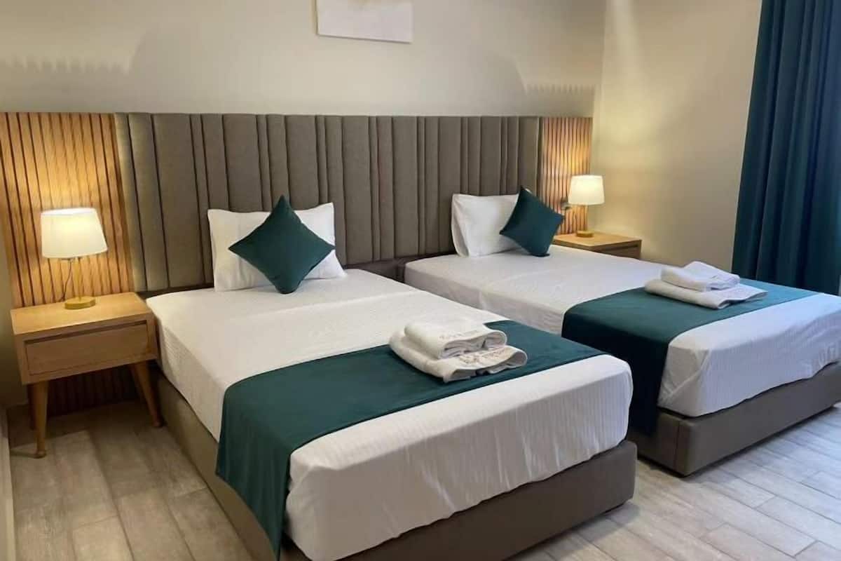 A hotel room with two beds, each with a pillow, a bedside lamp, and a folded towel on the bed.