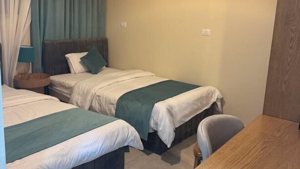 A room with two beds, a wooden desk, a chair, a lamp, and a wall-mounted painting. - Victoria (New Cairo City)