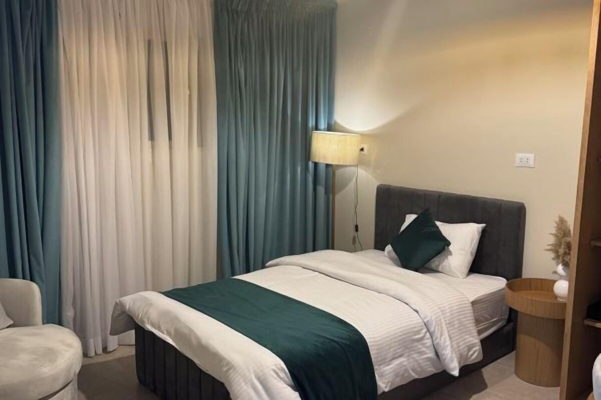 Une chambre d’hôtel avec un lit, une table de chevet, une lampe et des rideaux.