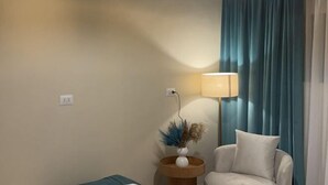 A room with a white armchair, a lamp, a vase with dried plants, and a blue curtain. - Victoria (New Cairo City)