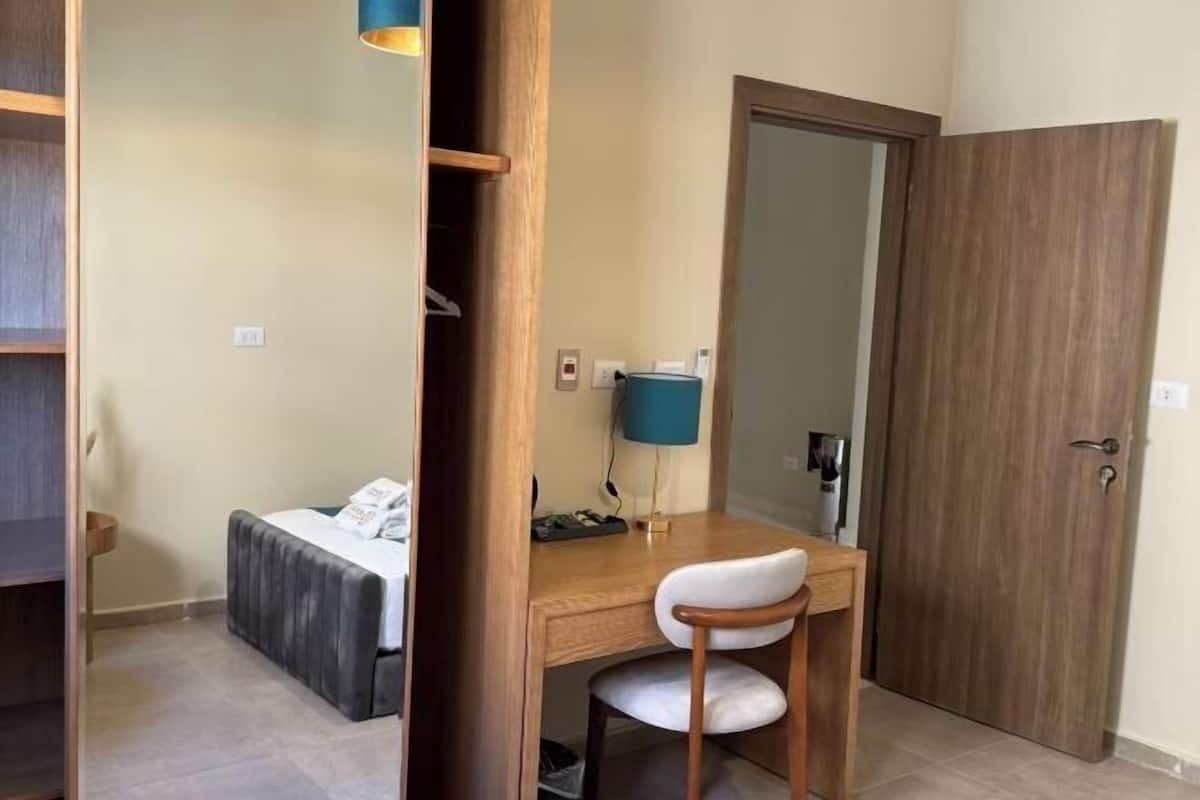 A bedroom with a bed, a desk with a chair, a wardrobe, and a mirror.