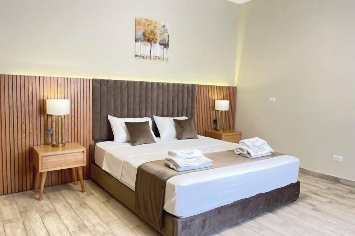 A hotel room with a large bed, two bedside tables with lamps, a wooden headboard, and a painting on the wall.