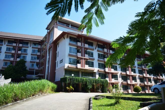 A multi-story hotel with a central courtyard, surrounded by greenery and palm trees.