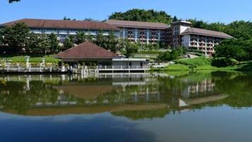 A hotel with a large building, a lake in front, and a small pavilion.