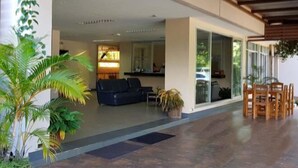 A spacious indoor area with a modern design, featuring a black sofa, wooden chairs, and potted plants. - Wanawes Mae Fah Luang (Chiang Rai)
