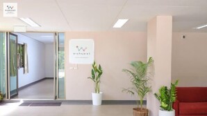 A reception area with a sign, potted plants, and a red couch. - Wanawes Mae Fah Luang (Chiang Rai)