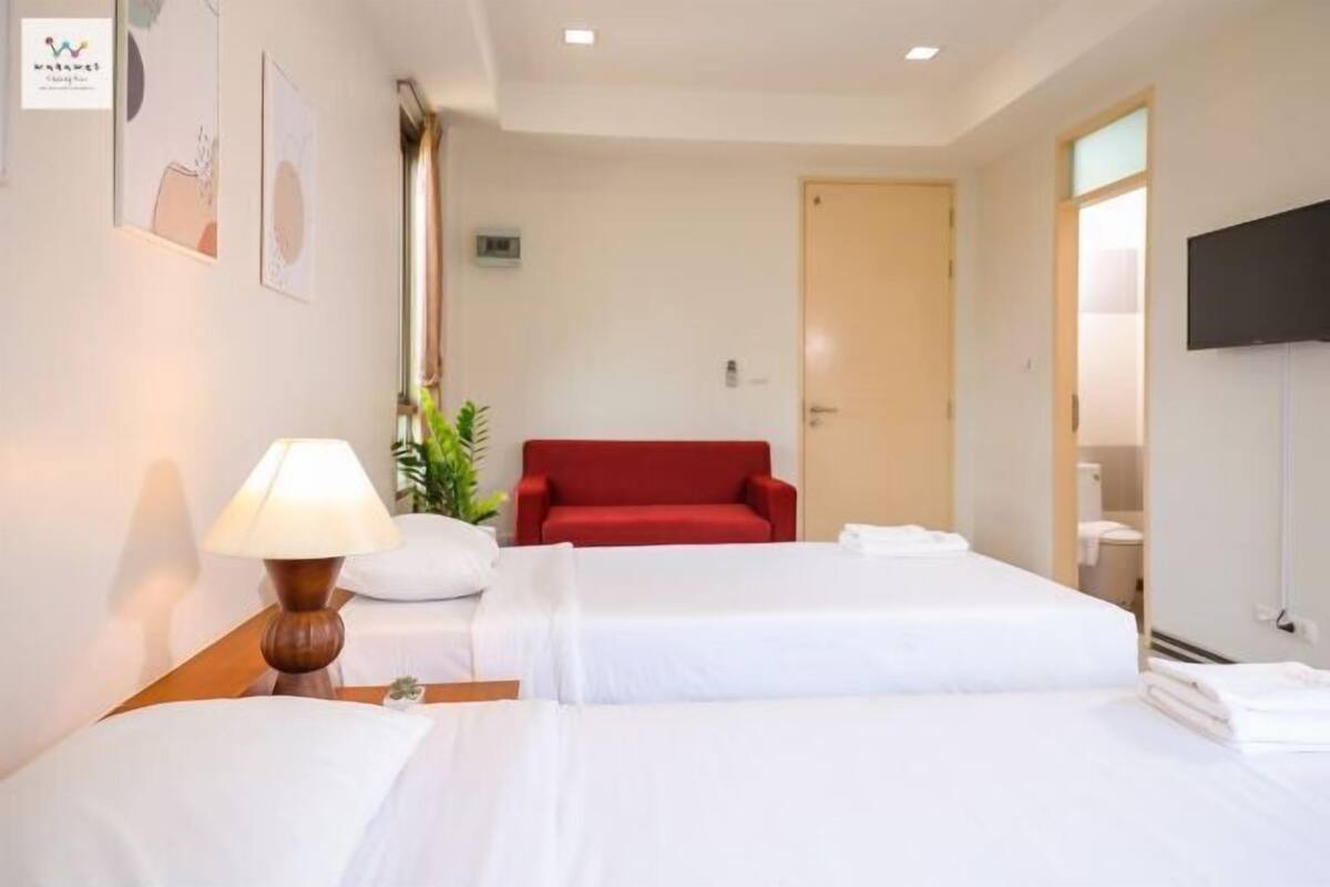 A hotel room with two beds, a red sofa, a TV, and a plant.
