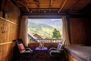 Una stanza in legno con un balcone, un letto, due sedie e un tavolo con un vaso.