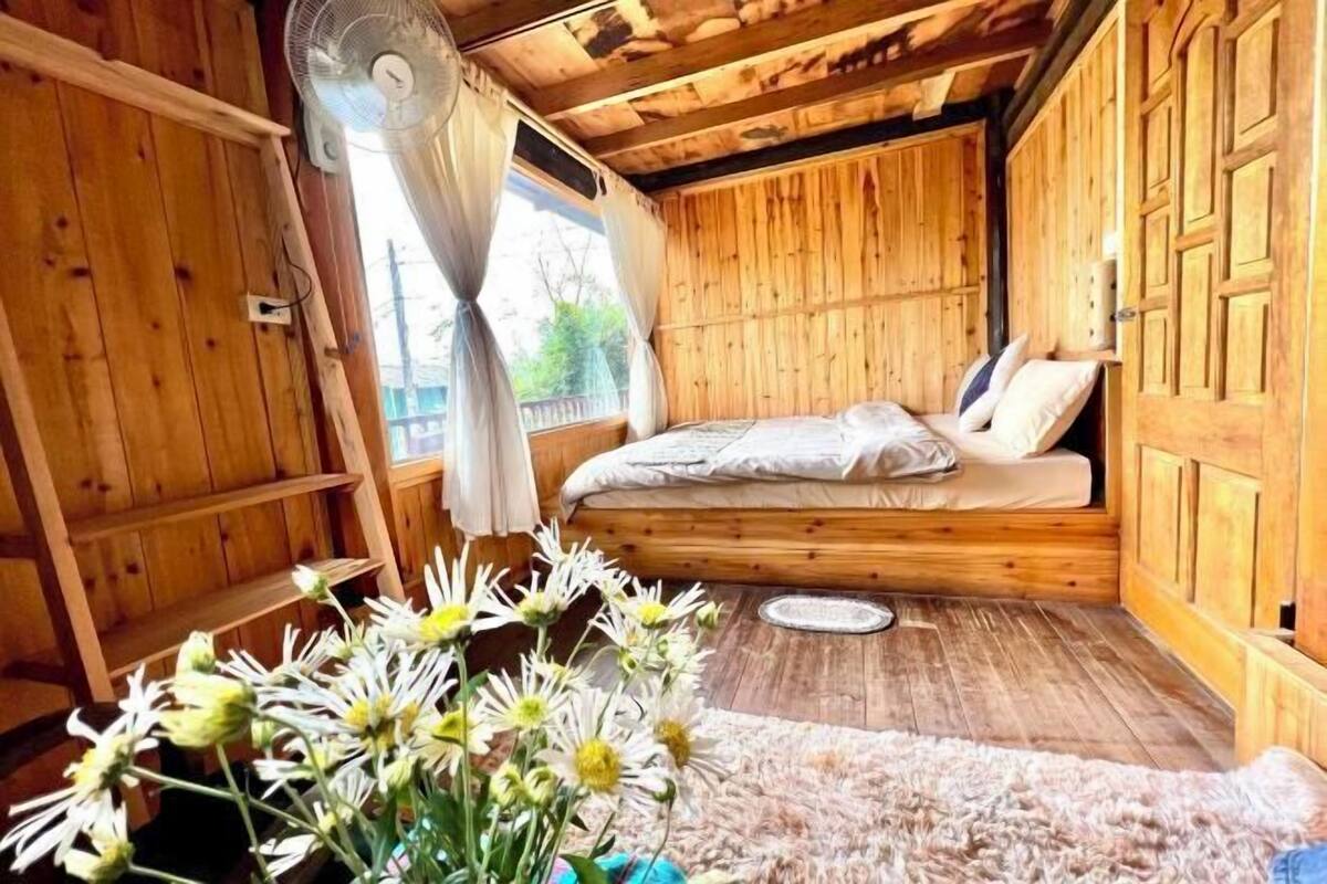Une chambre dans un chalet en bois, avec un lit, un ventilateur et une fenêtre avec des rideaux.