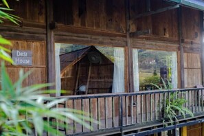 Una cabaña de madera con un balcón, un cartel que dice 'Desi House' y vistas del paisaje circundante.