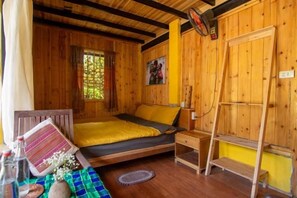 Una habitación de cabaña de madera con una cama, una mesita con una botella y una ventana.