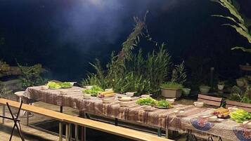 An outdoor dining area with tables set for a meal, surrounded by potted plants and a dark night sky.