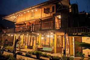 A two-story wooden building with a balcony, large windows, and outdoor seating area.