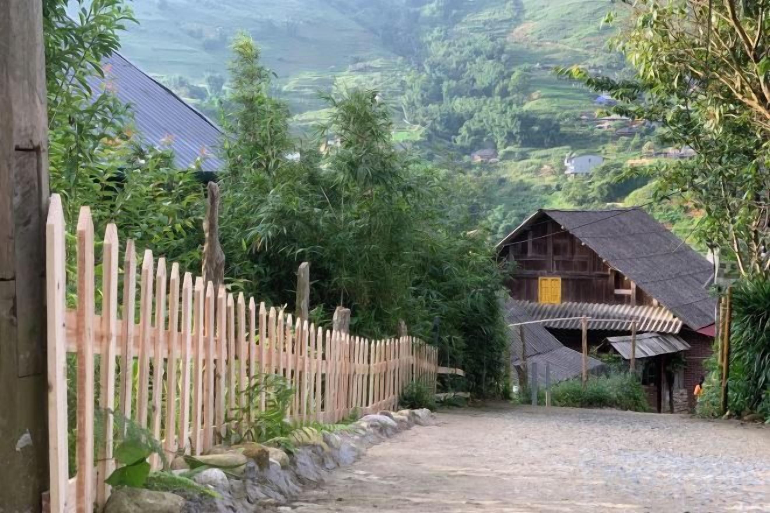 A rural setting with a wooden fence, a gravel path, and a rustic building with a sloped roof.
