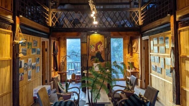 A cozy interior with wooden walls, a central seating area with chairs and tables, and a mural on the back wall. - Sapa Ta Van Desi House - Mountain View & Hiking Tours (Sapa)