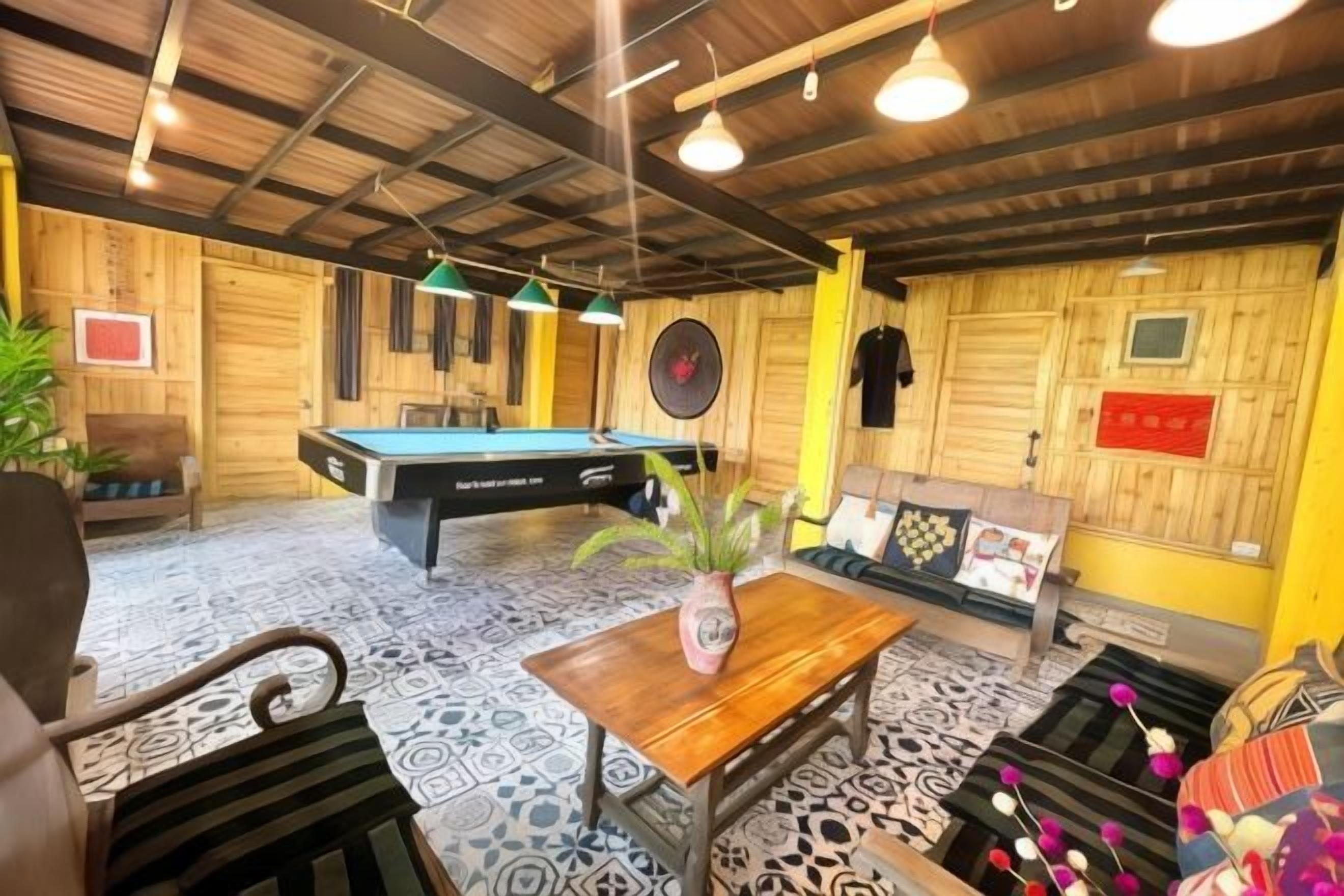 A room with a pool table, a billiards table, a sofa, and a table with a vase.