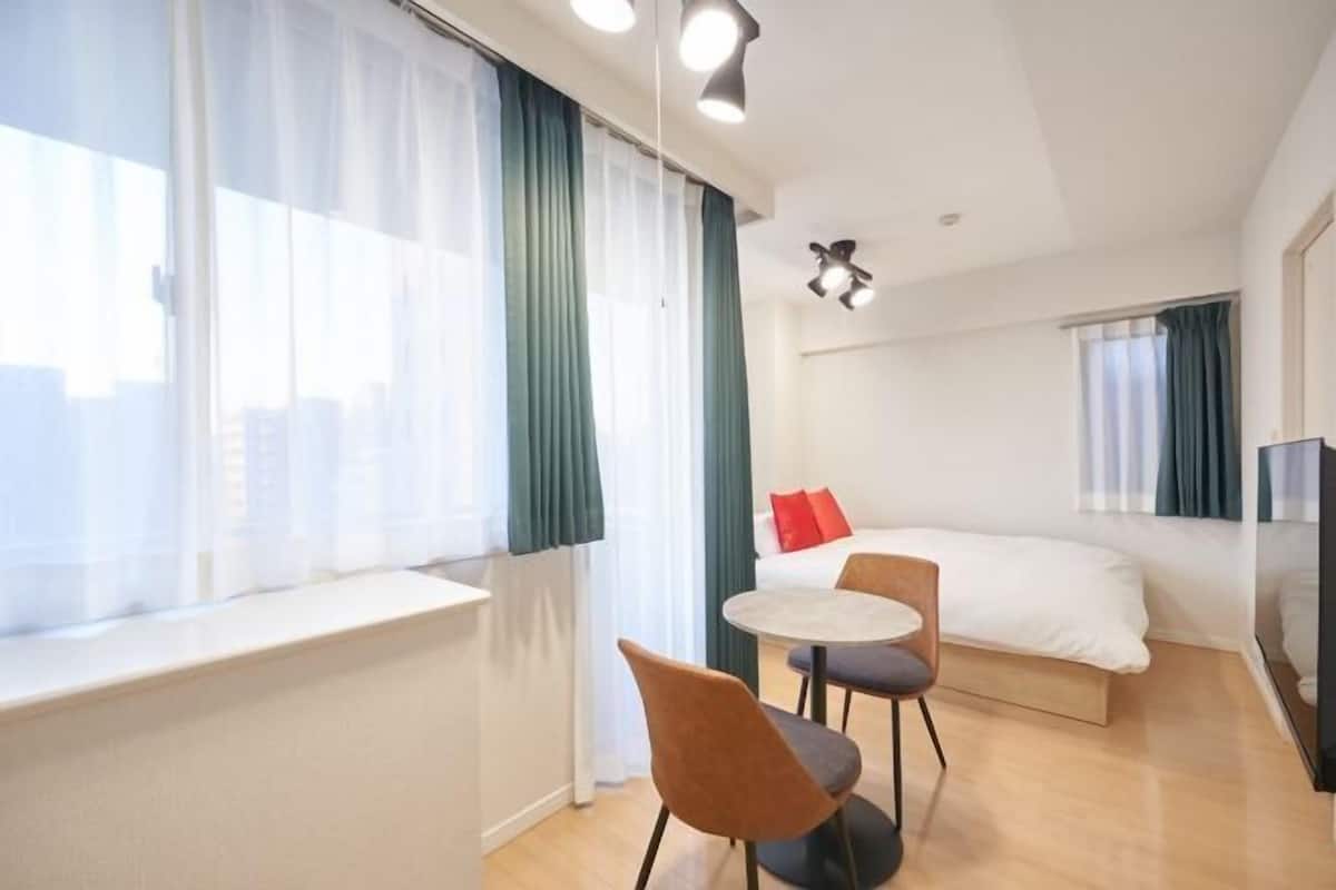 A hotel room with a bed, a small table with chairs, a TV, and a window with curtains.