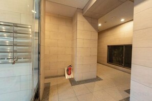 A corridor with tiled walls, a fire extinguisher, and a glass door with a metal handle. - Luce Takanawa (Tokyo)