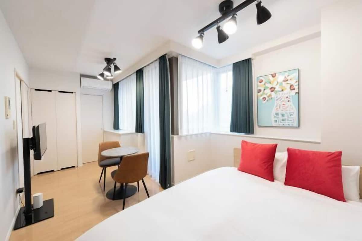 Ett hotellrum med en säng, ett skrivbord, en stol, en tv och ett fönster med gardiner.
