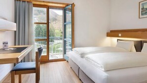 A hotel room with a bed, a desk, and a chair. There is a window with a view of trees and a building.