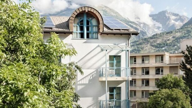 A building with a white facade, a balcony, and solar panels on the roof.