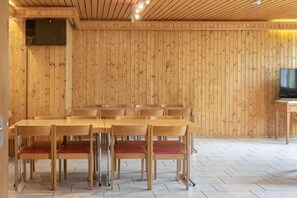 A wooden-paneled room with a dining table and chairs, a television on a stand, and a tiled floor. - St.Jodern (Visp)