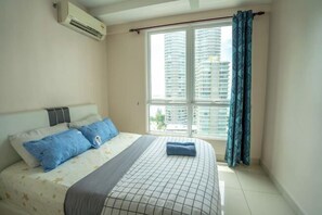 Ein Schlafzimmer mit Bett, Fenster mit Vorhängen und Klimaanlage.