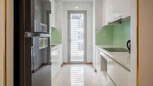 A narrow kitchen with white cabinets, a stainless steel refrigerator, and a green backsplash. - Gardenia Apartment Landmark (Ho Chi Minh City)