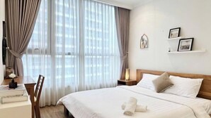 A hotel room with a large bed, a desk with a chair, a bedside table with a lamp, and a window with curtains. - Gardenia Apartment Landmark (Ho Chi Minh City)
