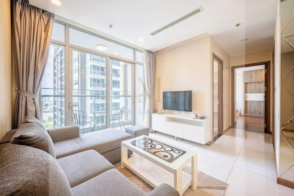 A modern living room with a sofa set, a coffee table, a TV, and a balcony with a view of buildings.