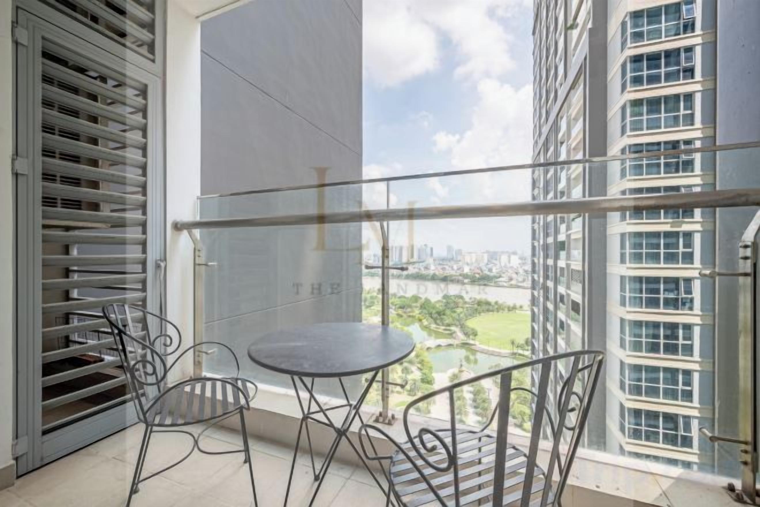 A balcony with a table and chairs, overlooking a cityscape with buildings and a river.