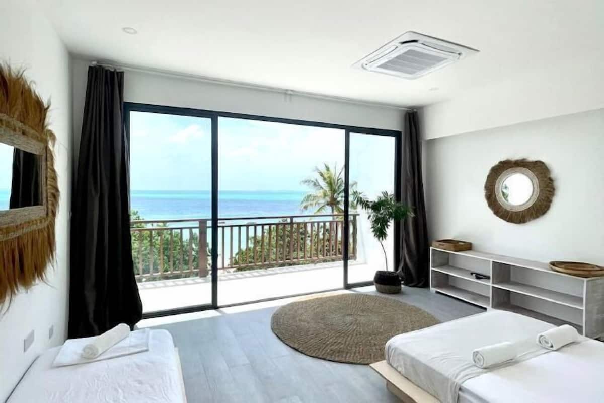 Ein Schlafzimmer mit zwei Betten, einem großen Fenster mit Meerblick, einem Balkon und einem runden Spiegel an der Wand.