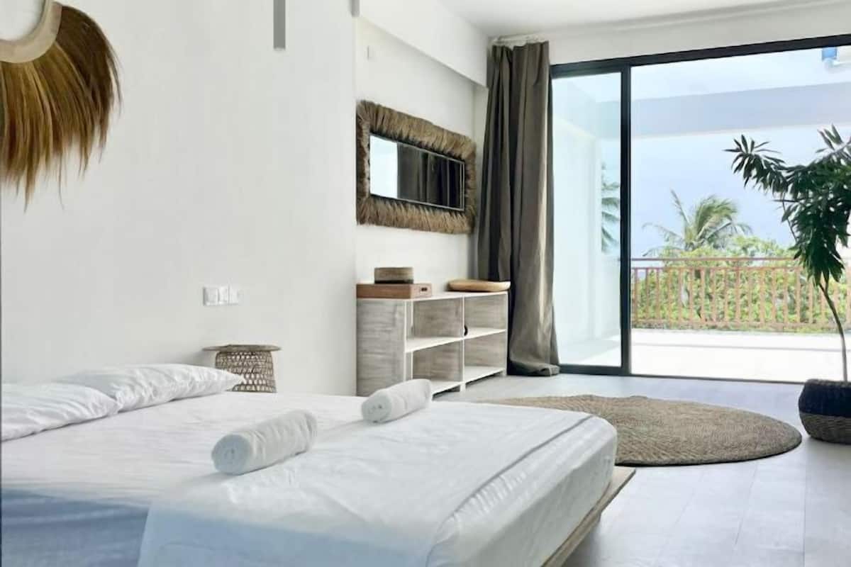 Ein modernes Schlafzimmer mit einem großen Bett, einem Spiegel, einer Pflanze und einem Balkon mit Blick.