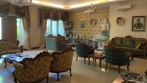 Ein traditionell eingerichteter Raum mit einer Chandelüster, Deckenventilator und strukturiertem Wandpapier. Es gibt zwei Sofas, einen Couchtisch und einen Beistelltisch mit Dekorationen.
