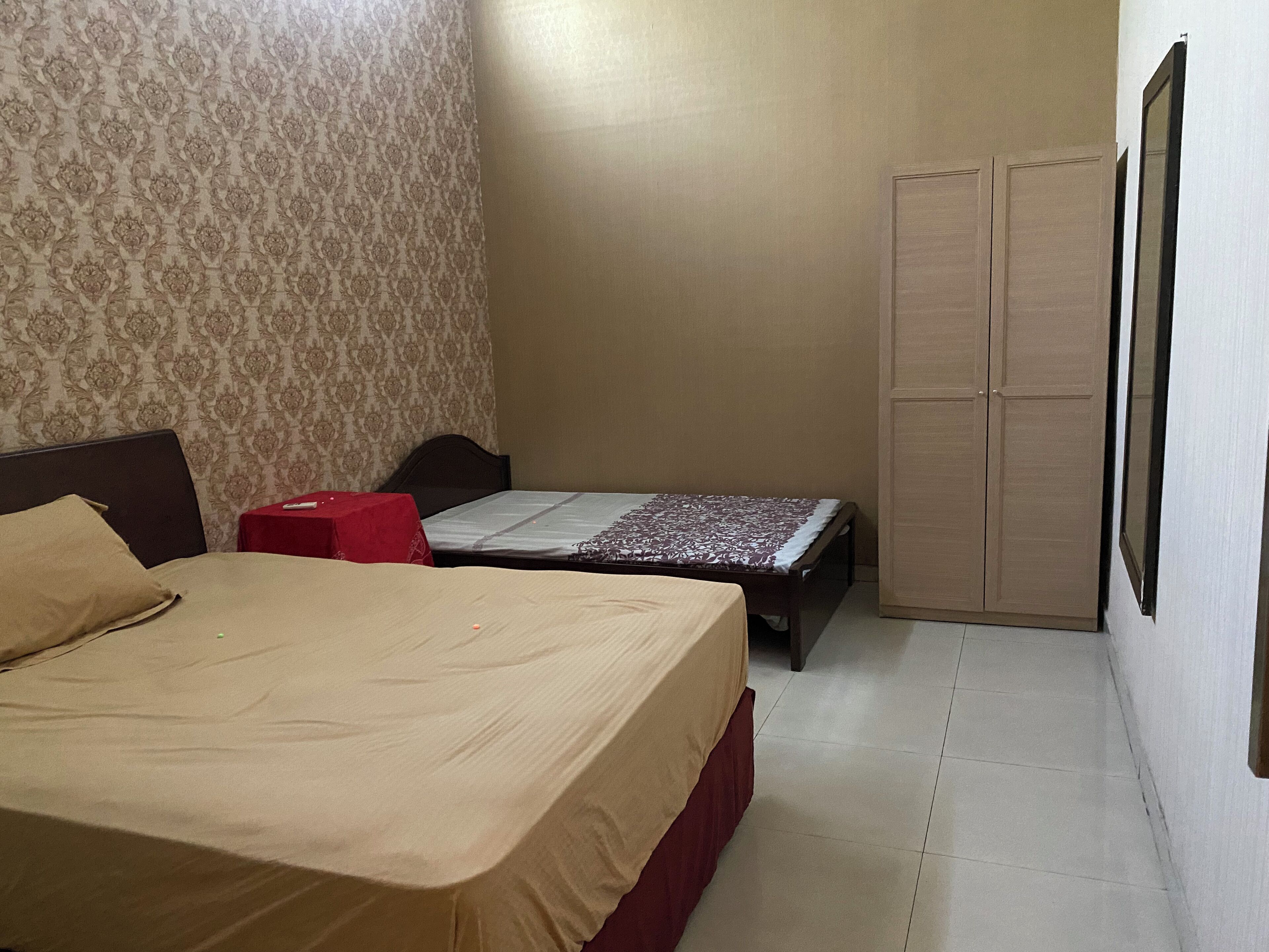 A bedroom with a bed, a small table, a wardrobe, and patterned wallpaper.
