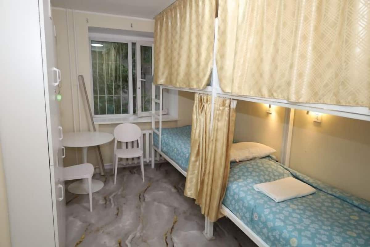 A bunk bed room with a window, a small table, and a chair.