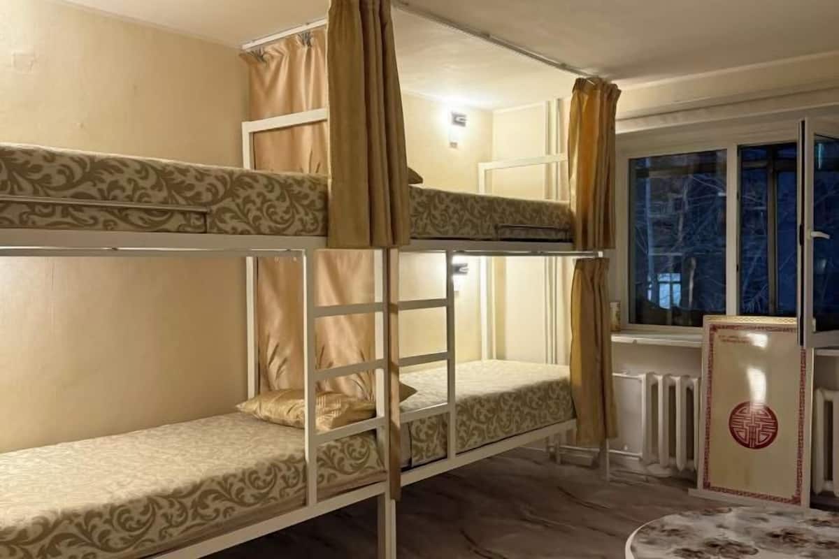 A bunk bed room with patterned bedding, a radiator, and a window with curtains.