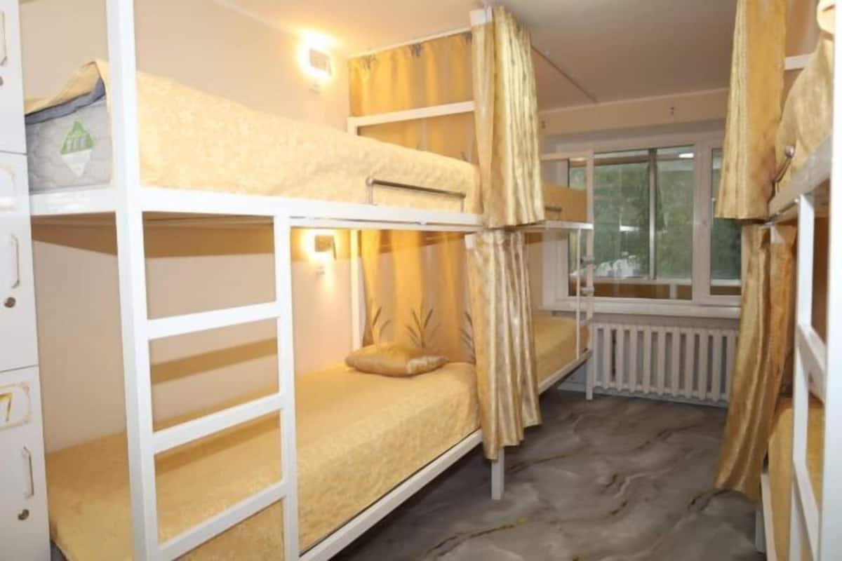 A bunk bed room with a window, curtains, and a radiator.