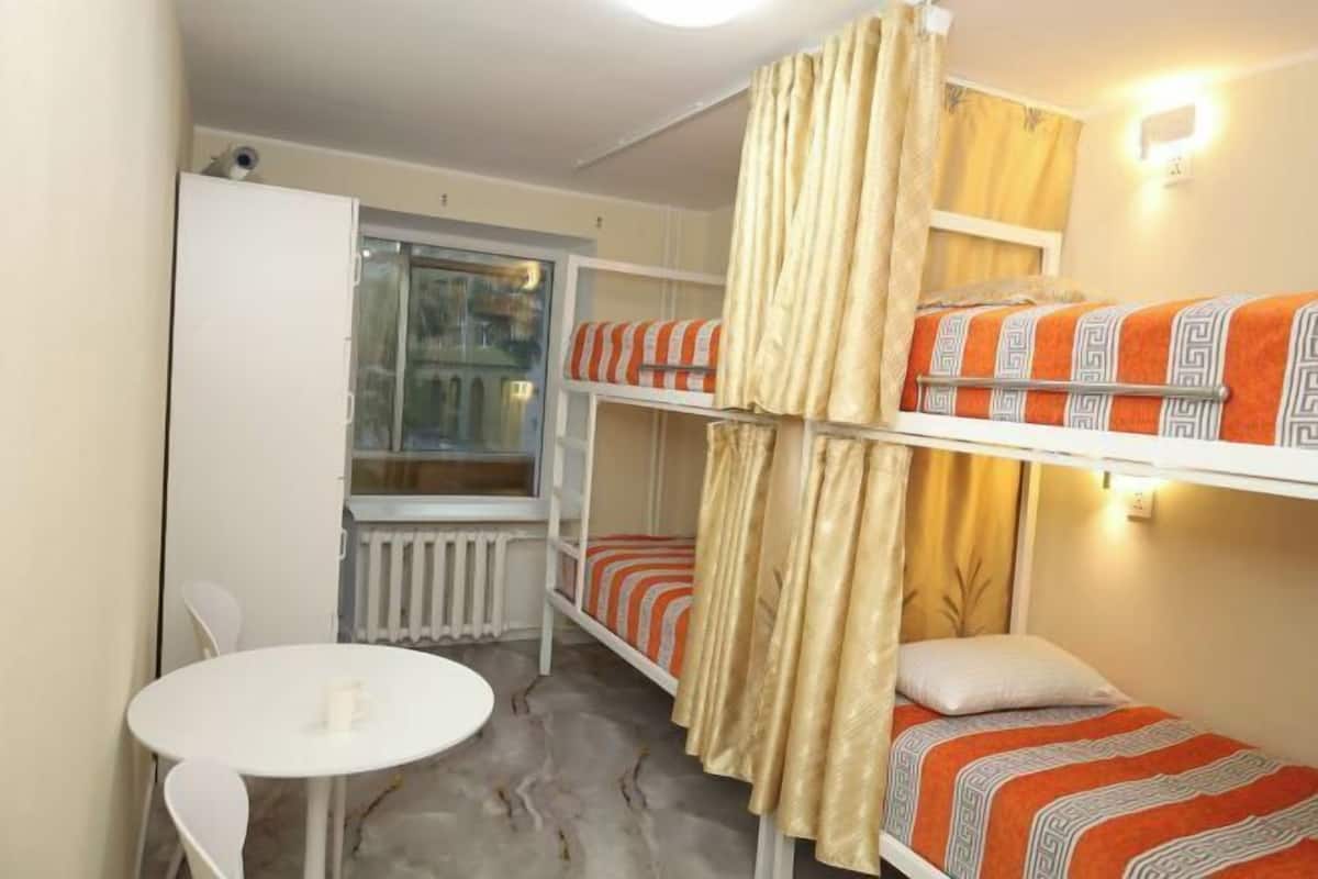 A bunk bed room with a window, a radiator, a table, and chairs.
