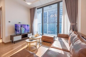 Un salon moderne avec un téléviseur à écran plat, un canapé, une petite table et une grande fenêtre avec des rideaux.