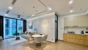 Een moderne woonkamer met een bank, eettafel en stoelen, een keuken met kasten en apparatuur, en grote ramen met uitzicht.