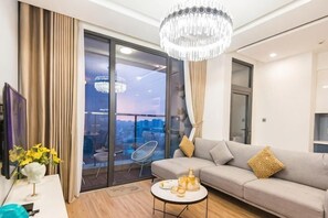 A modern living room with a sofa, a coffee table, a chandelier, and a city view through large windows. - Suites Housing Vinhomes Metropolis Hanoi (Hanoi)
