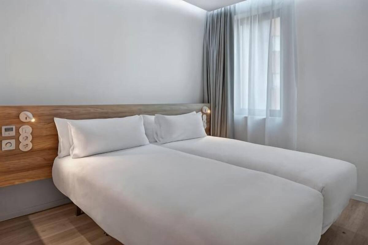 A double bed with white bedding, a wooden headboard, and a bedside table with a lamp.