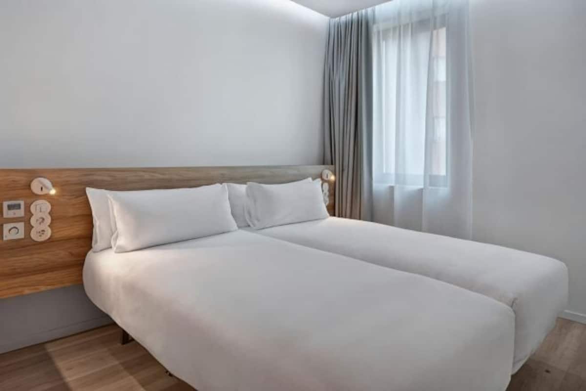 Uma cama de casal com roupa de cama branca, cabeceira de madeira e mesa de cabeceira com abajur.